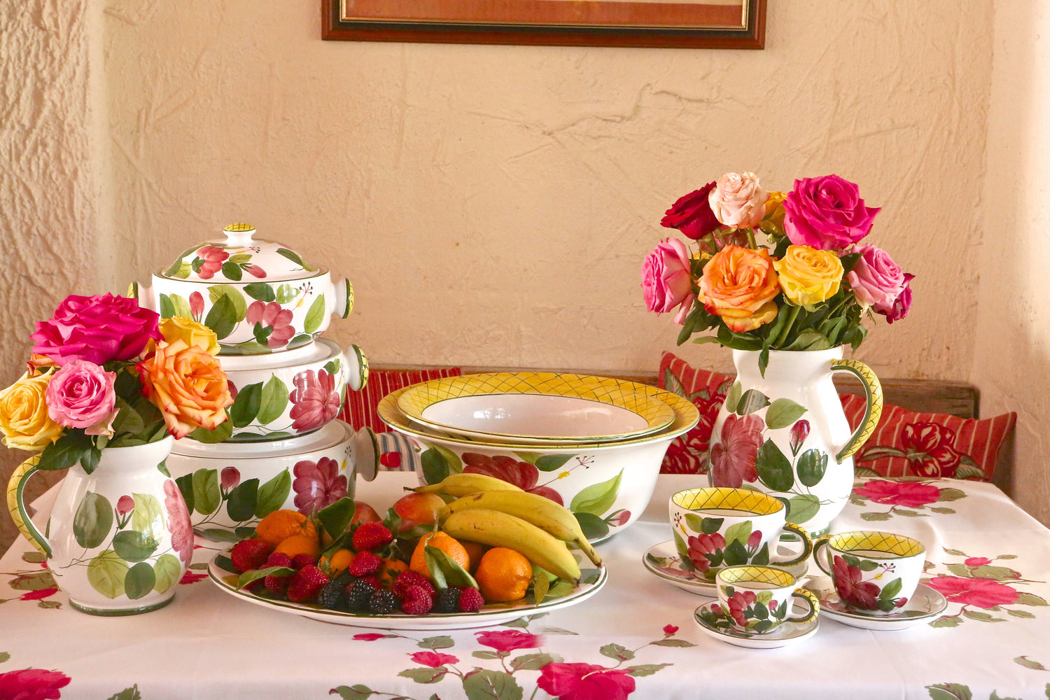Hand-painted Hibiscus pattern table the Ivy tableware with ceramic pitchers, bowls, and teacups in a vibrant summer table setting with fruit and roses.