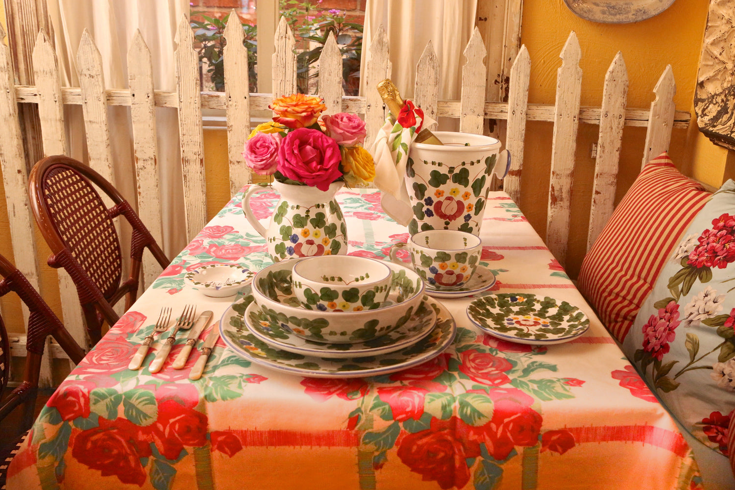 The Ivy at Home's classic Ivy pattern ceramic tea set with green clovers and colorful flowers, styled with a floral pitcher of roses on a cozy indoor table.