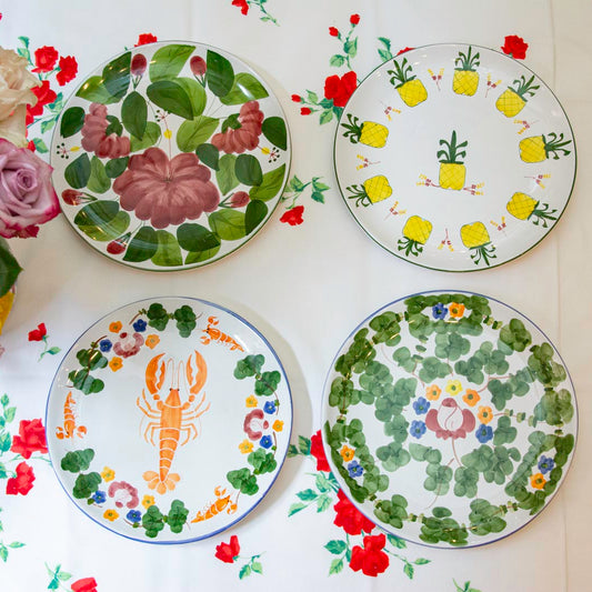 Set of four decorative plates with floral and animal designs on a floral-patterned tablecloth.